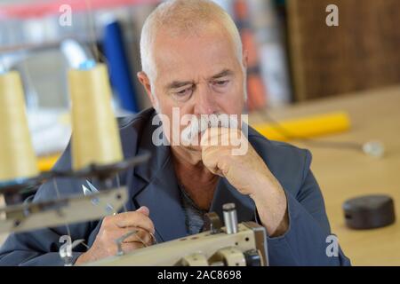 pensive senior man using industrial sewing machine Stock Photo
