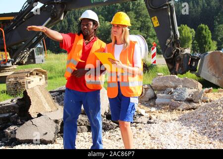 Male and Female construction workers analyzing plans on a construction site Stock Photo