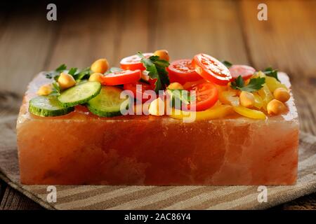 Vegetable salad on pink salt block on stripe napkin and wooden background Stock Photo