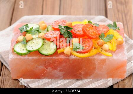 Vegetable salad on pink salt block on stripe napkin and wooden background Stock Photo