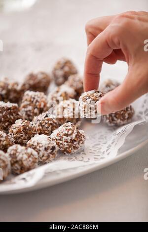 White plate full of delicious raw protein balls. Healthy sweets for sport people. A hand taking homemade dessert. Stock Photo