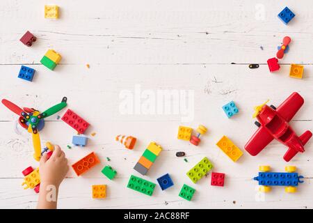 The kid boy plays in multi-colored cubes on a white wooden table. Top view on colored toy bricks. Stock Photo