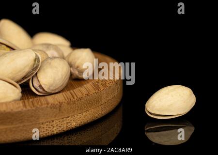 Lot of whole salted pistachio on round bamboo coaster isolated on black glass Stock Photo