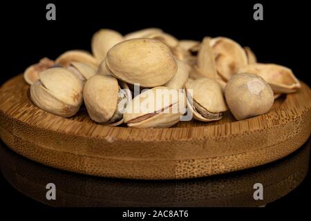 Lot of whole salted pistachio on round bamboo coaster isolated on black glass Stock Photo