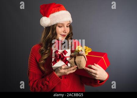 A beautiful model in a Santa Claus hat and a red knitted sweater holds many gifts in her hands. The concept of new Year, Christmas gifts, giving, Christmas shopping. Template for your advertising. Stock Photo
