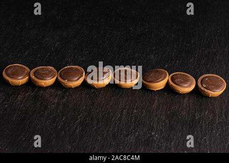 Group of eight whole sweet brown toffee in line on grey stone Stock Photo