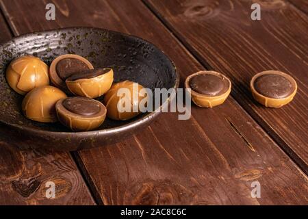 Group of eight whole sweet brown toffee in glazed bowl on brown wood Stock Photo