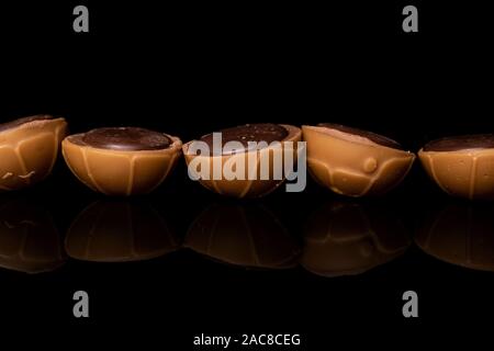 Group of five whole sweet brown toffee in line isolated on black glass Stock Photo