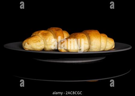 Group of two whole sweet golden mini croissant on gray ceramic plate isolated on black glass Stock Photo