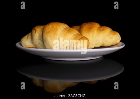 Group of two whole sweet golden mini croissant on white ceramic plate isolated on black glass Stock Photo