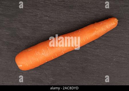 One whole fresh orange carrot flatlay on grey stone Stock Photo