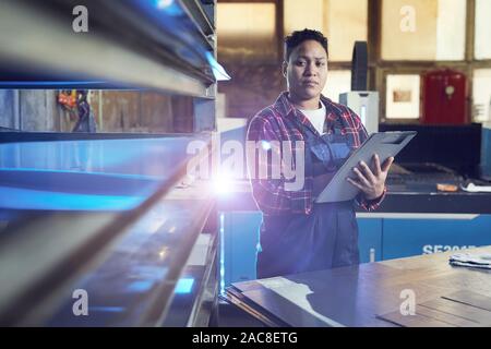 Waist up portrait of contemporary female worker writing on clipboard while watching production process at factory, copy space Stock Photo