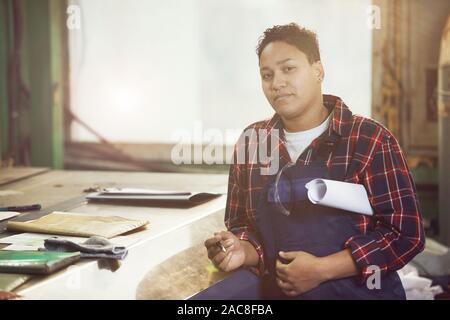 Portrait of mixed-race female engineer looking at camera while studying blueprint plants and production factory, copy space Stock Photo