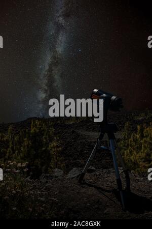Young man observes starry sky through a telescope. Mountains, surrouded by pine tree forest in the background night landscape with colorful Milky Way Stock Photo