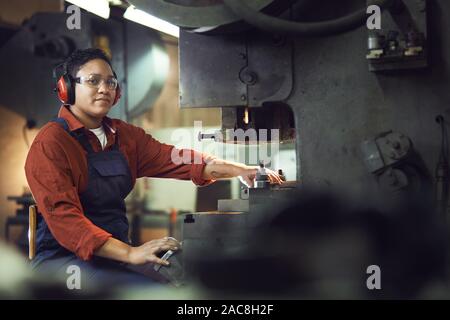 Portrait of smiling African-American woman looking at camera while operating machine units at industrial factory, copy space Stock Photo