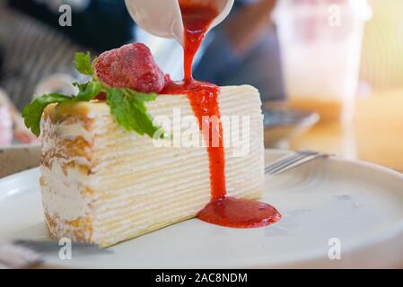Crape cake slice with strawberry sauce on white plate on the table background / Piece of cake with whipped cream Stock Photo