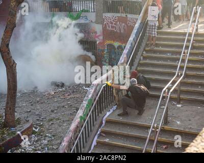 Santiago Chile NOV 12th / first line protestors fight against the police forces that are hidden behind the metal doors, trowing tear gas bombs Stock Photo
