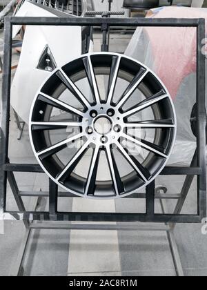 A two colored black and silver painted aluminum alloy wheel is mounted on a special frame during drying in a chamber in a vehicle body repair workshop Stock Photo