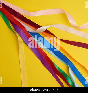 many silk multi-colored ribbons on a yellow background, top view Stock Photo
