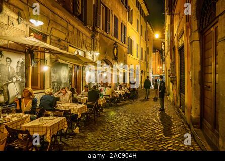 A typical residential street in Rome, where people are dining outdoors at a small neighborhood restaurant on a cobblestone street. Stock Photo