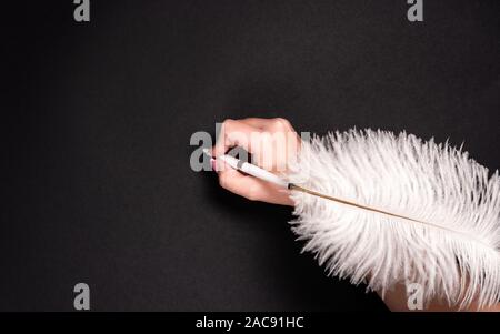 Female hand holding feather pen over black background Stock Photo