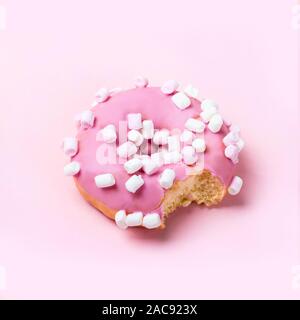 Bitten pink icing donut with marshmallows on pink background. Minimal concept. Stock Photo