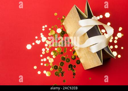 Gold Paper shopping bag and trendy hexagonal sparkles on red background. Holiday sale concept. Stock Photo