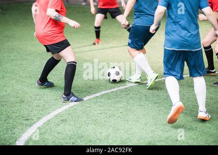 Two female football teams in red and blue sports uniform running down green field while attacking ball during game Stock Photo