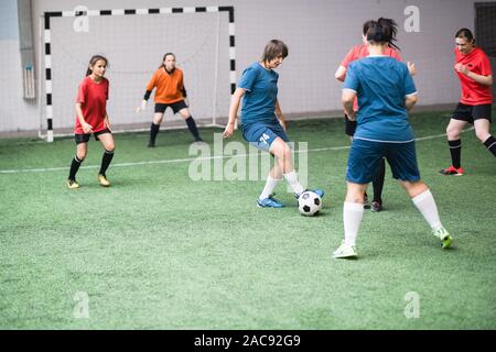 Young active female players in blue and red sportswear attacking soccer ball during game of football on the filed Stock Photo