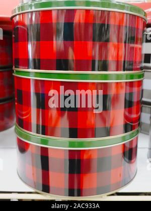 Three red and black plaid Christmas gift tins with green lids stacked on a shelf in a craft store. Lower Mainland, British Columbia, Canada Stock Photo