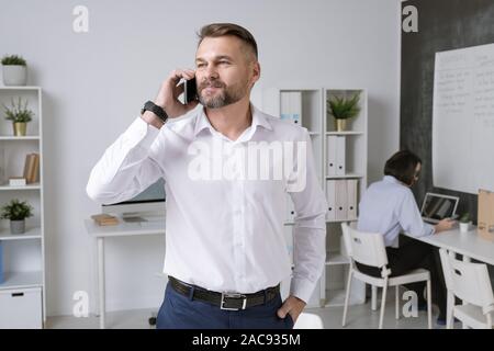 Confident entrepreneur with smartphone consulting one of his employees while standing in office Stock Photo