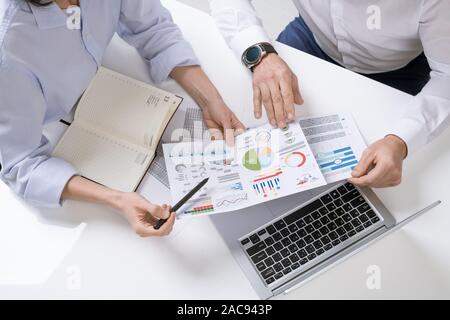 Hands of two contemporary brokers discussing financial documents with graphs, charts and diagrams at meeting Stock Photo