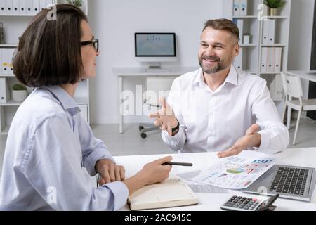 Happy mature broker and his young female colleague discussing financial documents in office Stock Photo