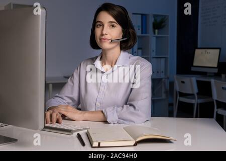 Pretty young customer support representative with headset speaking to clients online and answering their questions Stock Photo