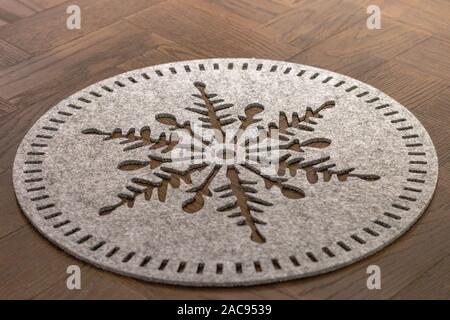 A light grey wool felt round dish mat in a shape of a flake of snow lying on a dark wooden table Stock Photo