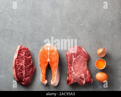 Carnivore or keto diet concept. Raw ingredients for zero carb or low carb diet - rib eye, salmon steak, pork, egg on gray stone background. Top view or flat lay. Copy space top. Stock Photo