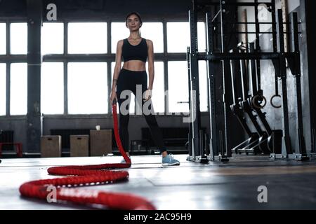 Battle rope, fitness and woman in studio for exercise, strength training  and cardio workout burning calories. Wellness, focus and healthy girl in a  squat pose moving ropes with a blue background Stock