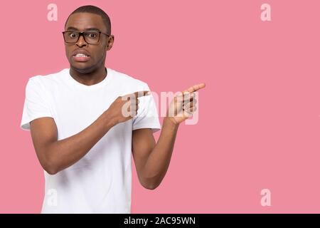 Nervous African American man in glasses pointing fingers at copy space, doubtful client customer demonstrating shopping offer, looking at camera, feel Stock Photo