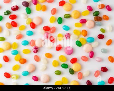 Many scattered colorful sweets, candies, lollipops on  white background, top view. Jelly beans. Stock Photo