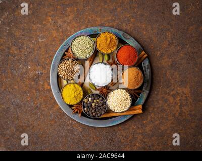 Mix spices on round metal plate - coriander seeds, ground red pepper, salt, black pepper, rosemary, turmeric, curry. Top view, close up, metall rusty Stock Photo