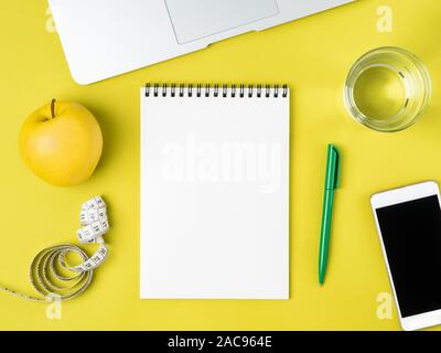 Blank Notebook page for Diet plan or menu, tape measure, water in glass and apple on bright yellow background, weight loss concept, top view. Stock Photo