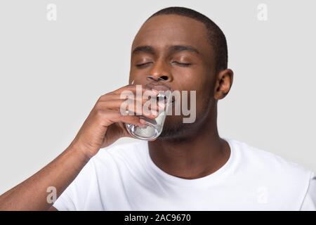 Healthy thirsty African American man drinking clean, enjoying mineral water with closed eyes, handsome young male holding glass, feeling dehydrated, c Stock Photo