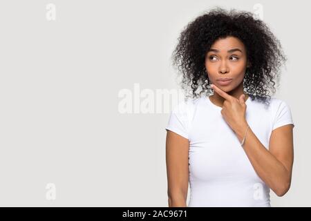 Thoughtful African American woman touch chin with finger, pensive young female looking aside at copy space, pondering special offer, shopping sale, ma Stock Photo