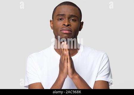 Upset African American man join hands in prayer with hope, worried unhappy young male asking for help with problems, religious Christian looking at ca Stock Photo