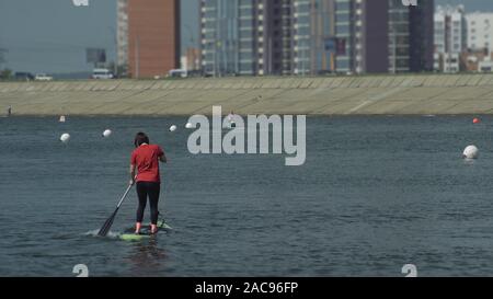Athlete on stand up paddleboard sup holding paddle board up in air in success on paddleboarding race. SUP surfboard surfing, water sport. Stock Photo