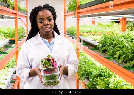 Young smiling female greenhouse worker with stack of containers Stock Photo