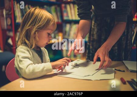 A teacher is supervising a little toddler using scissors at school Stock Photo