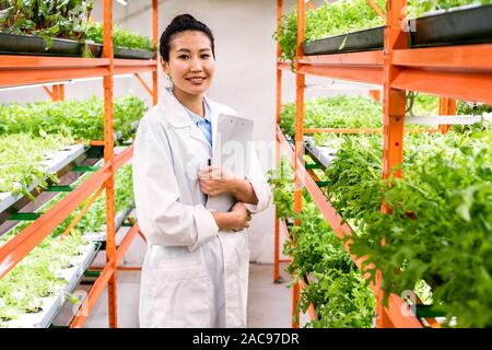 Young successful female researcher or agronomist in whitecoat standing in aisle Stock Photo