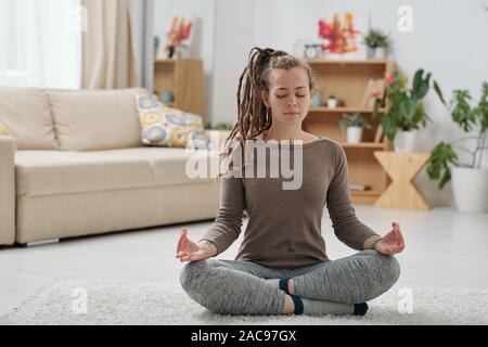 Pretty young female in activewear sitting on the floor with crossed legs Stock Photo