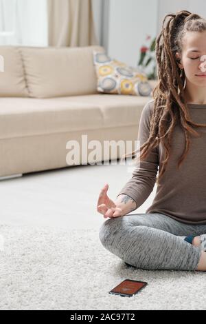 Girl in activewear sitting on the floor with legs crossed and hands on her knees Stock Photo